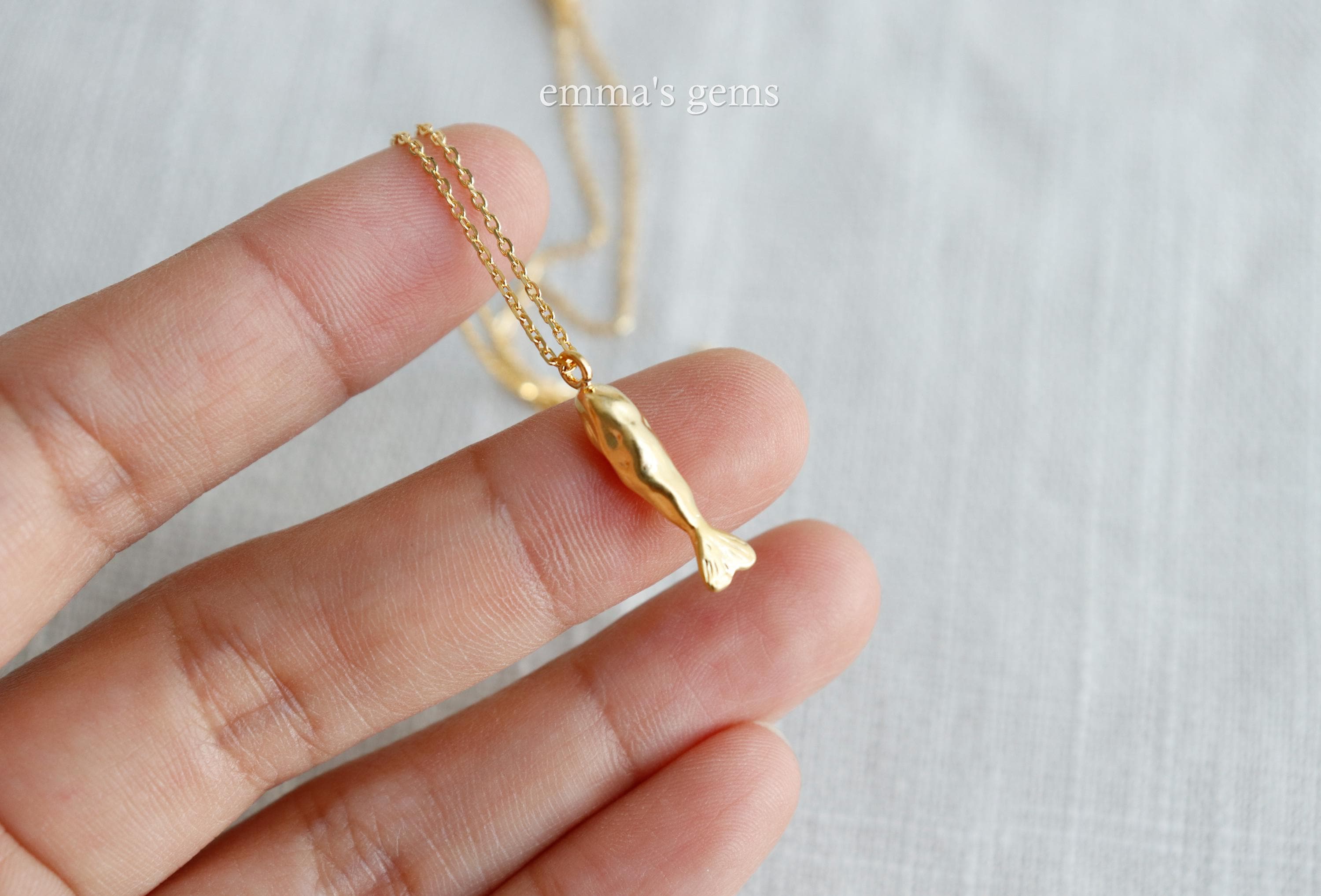 Gold necklace with a fish pendant held by a hand on a light background