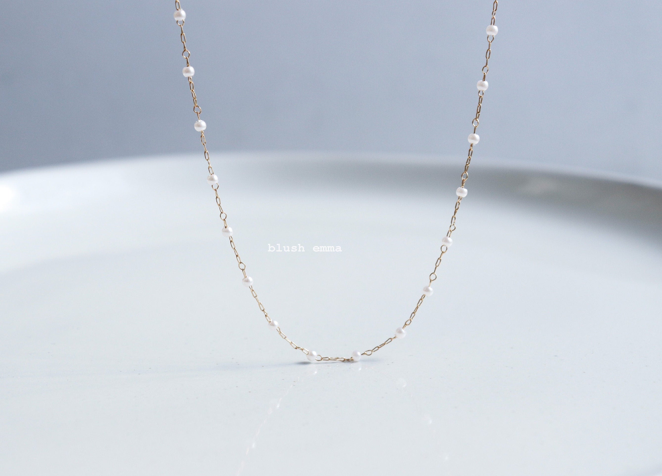 spaced pearl necklace by blushemma. Delicate gold chain necklace on a light gray background