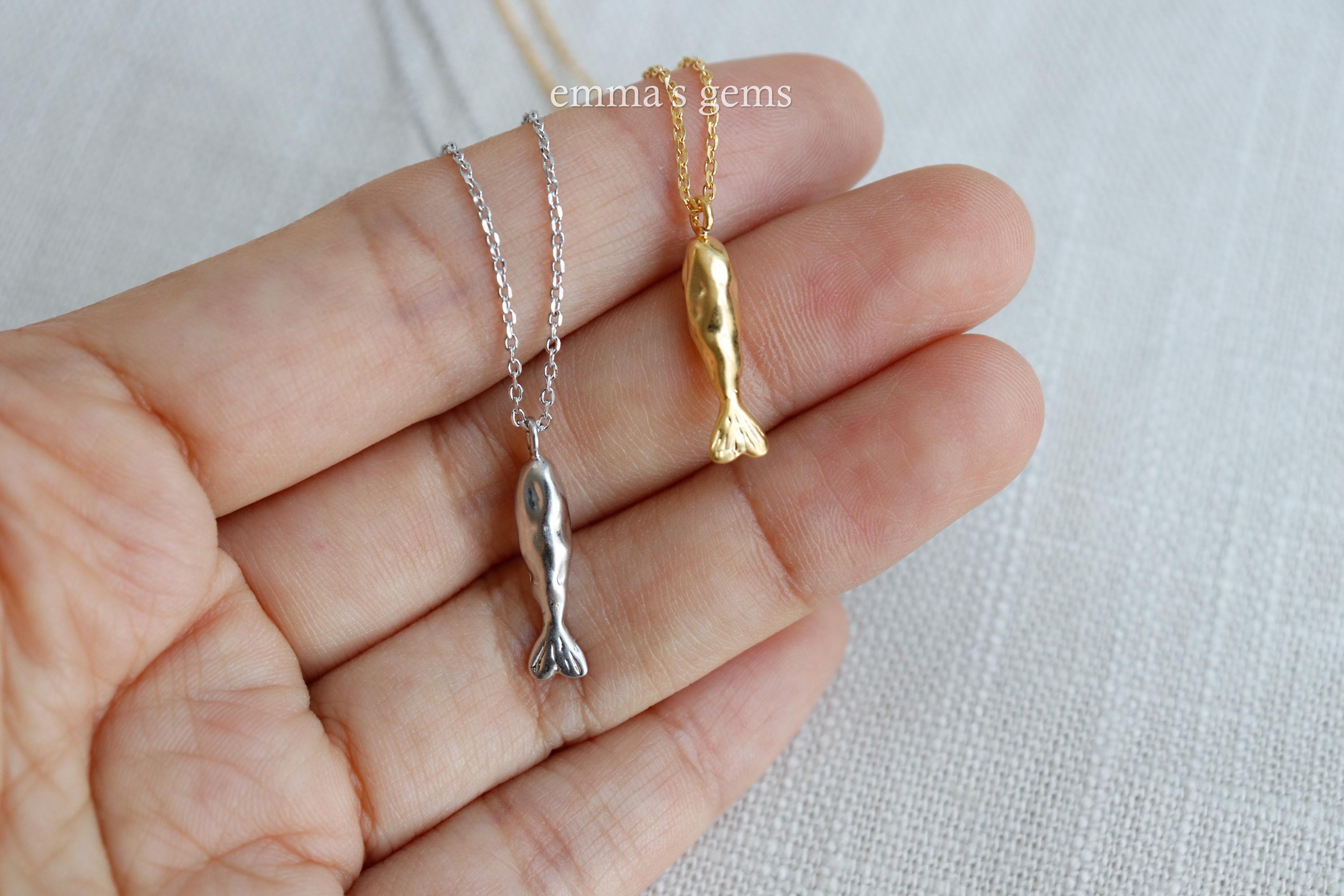 Gold and silver fish-shaped pendants on a hand with 'emma's gems' branding.
