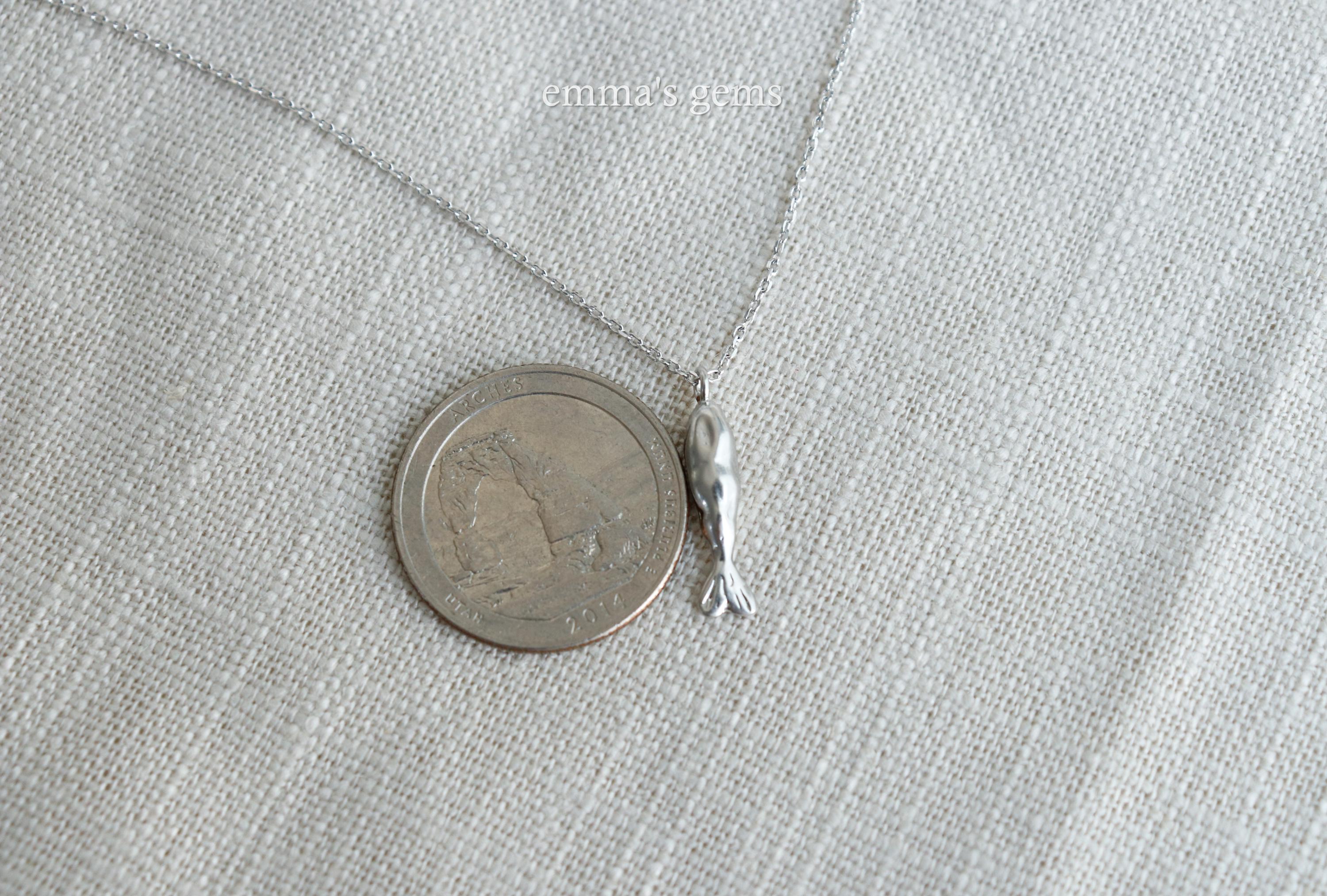 Small silver fish pendant next to a coin on a light gray fabric background