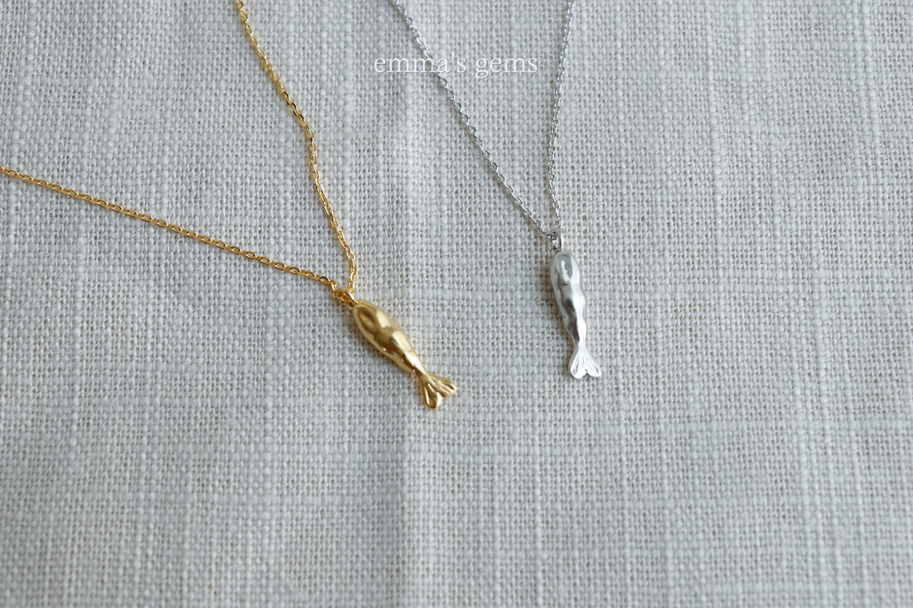 Gold and silver necklaces with fish pendants on a textured gray background