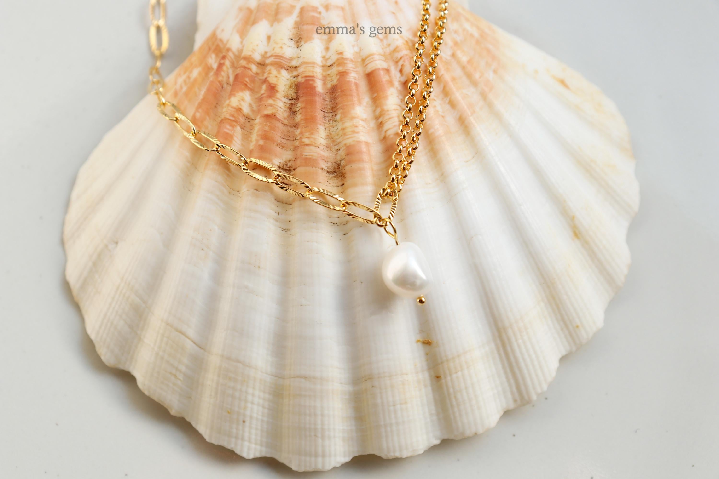 Gold necklace with a pearl pendant on a seashell against a light background