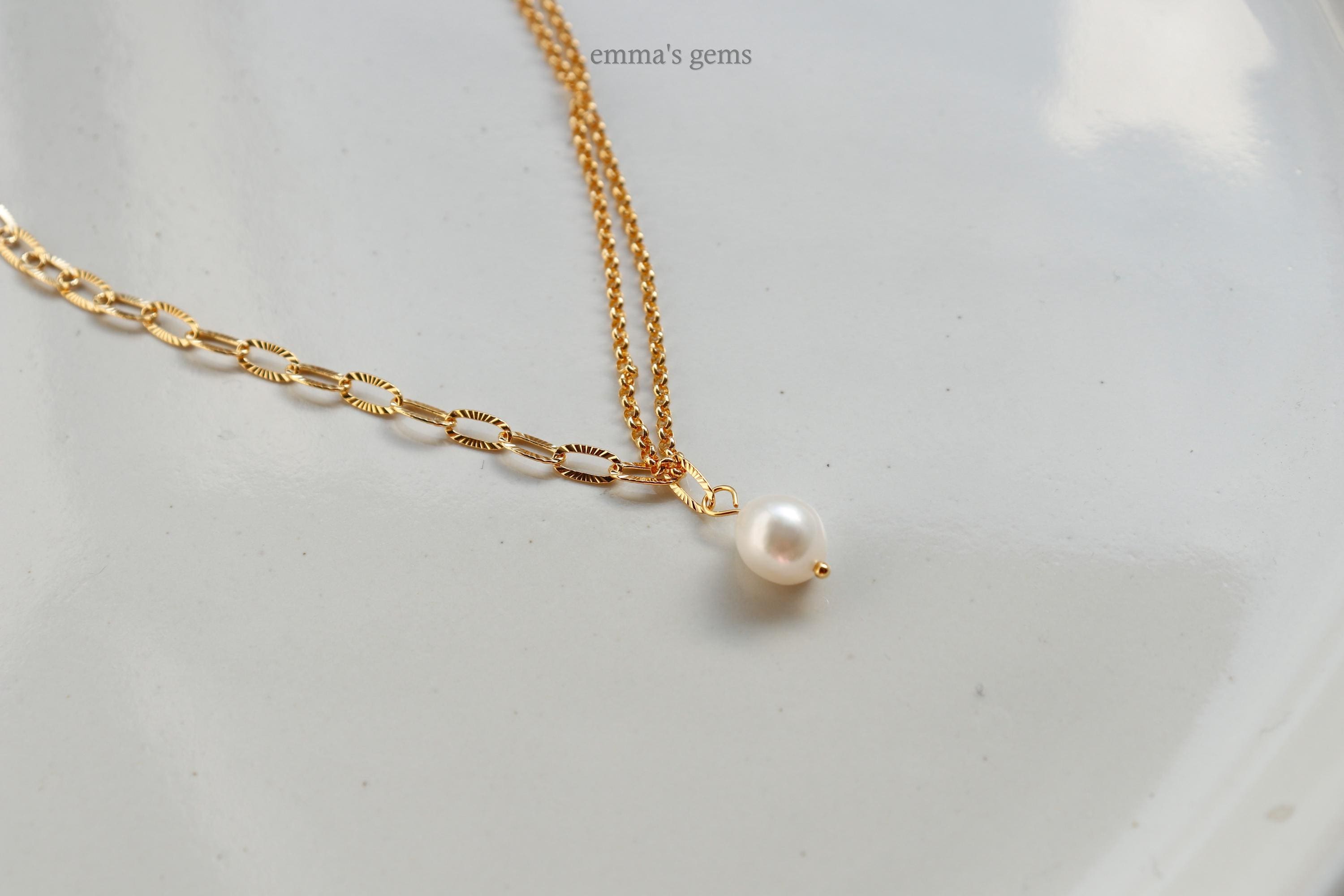 Gold chain necklace with a single pearl pendant on a light gray background