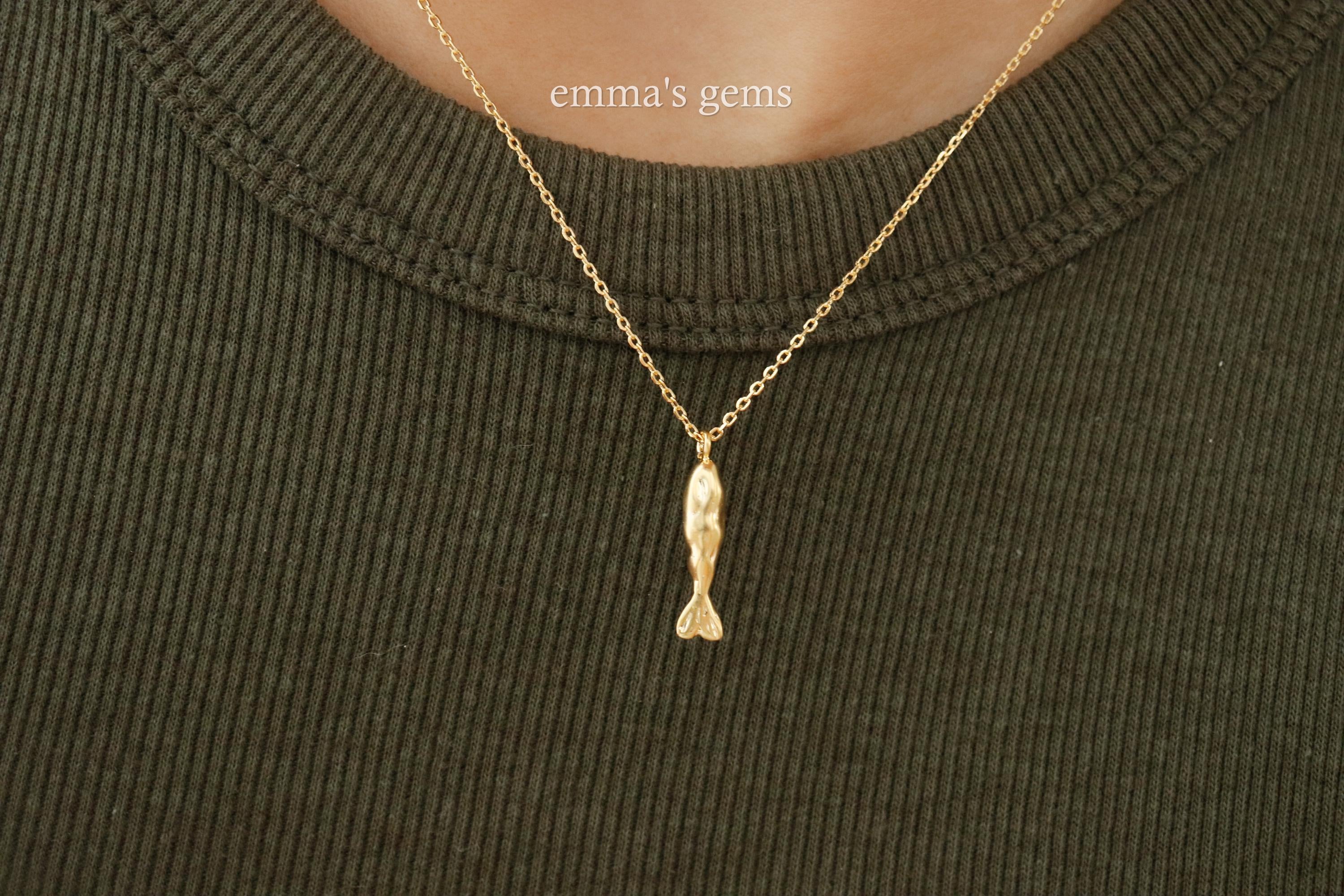 Gold fish-shaped pendant necklace on a green sweater with 'emma's gems' branding.