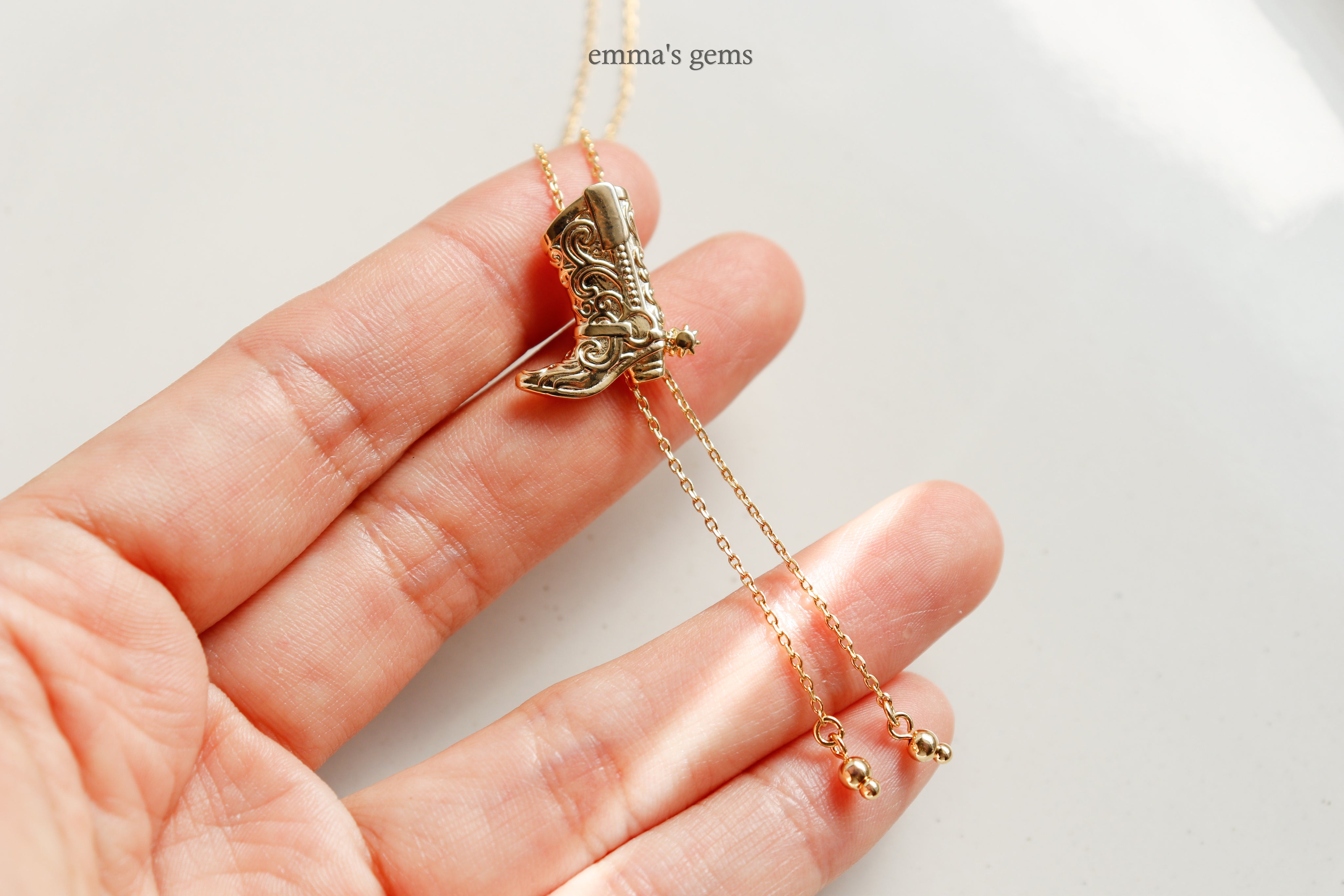 Gold necklace with a boot pendant held in a hand against a white background