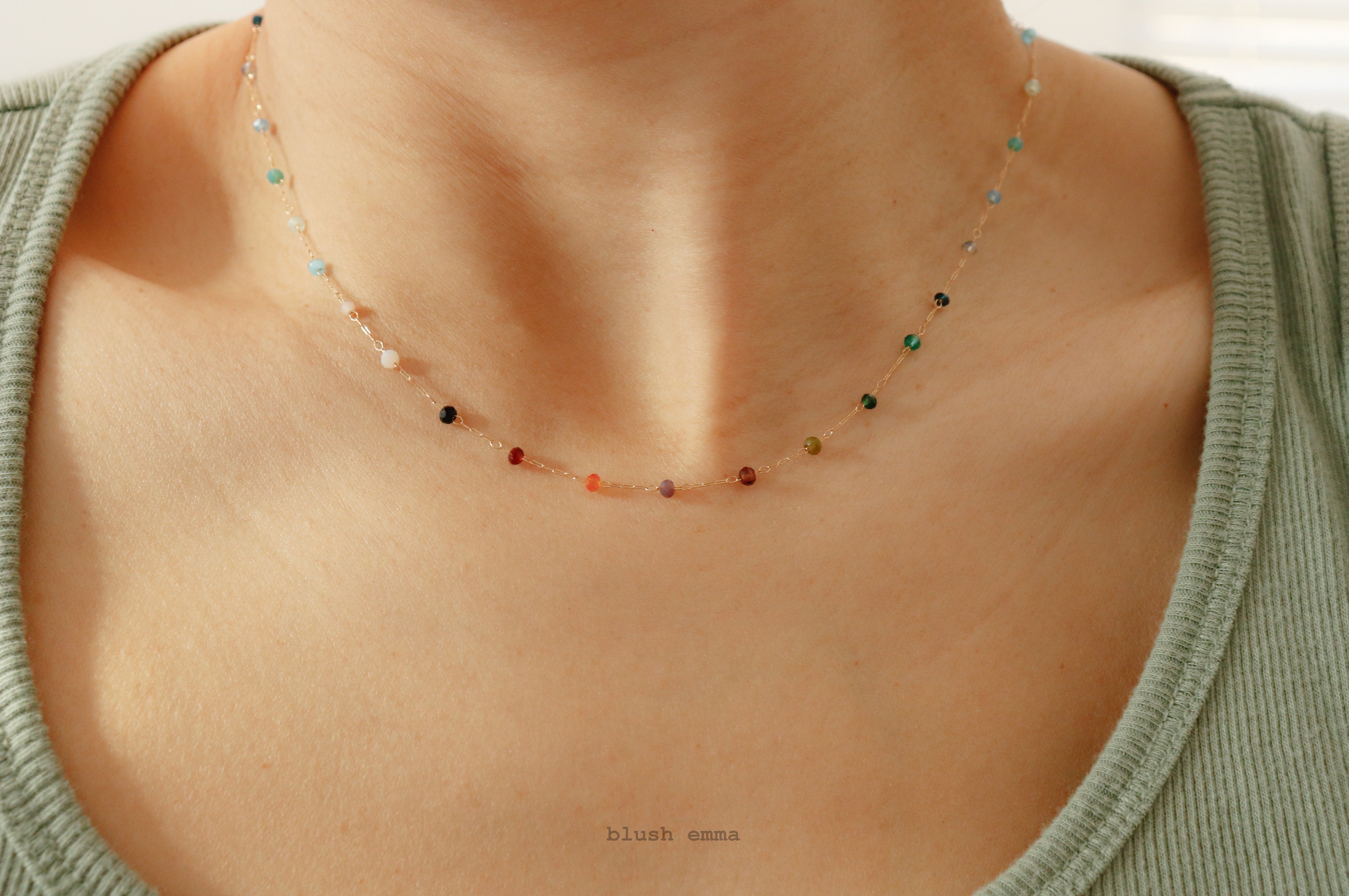 Necklace with small rainbow beads worn by a person in a green top