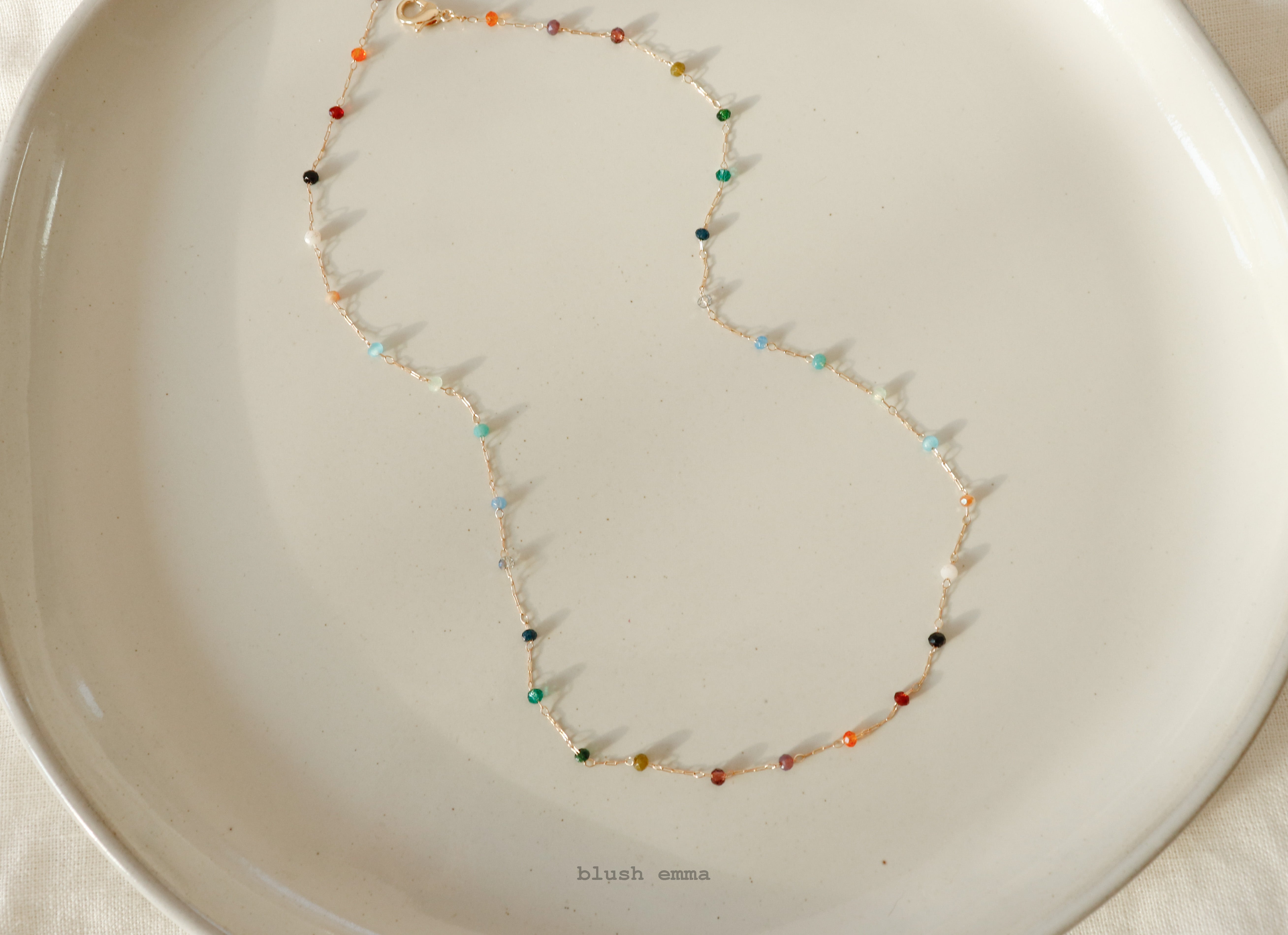 Necklace with multicolored beads on a white dish, brand 'blush emma' visible.