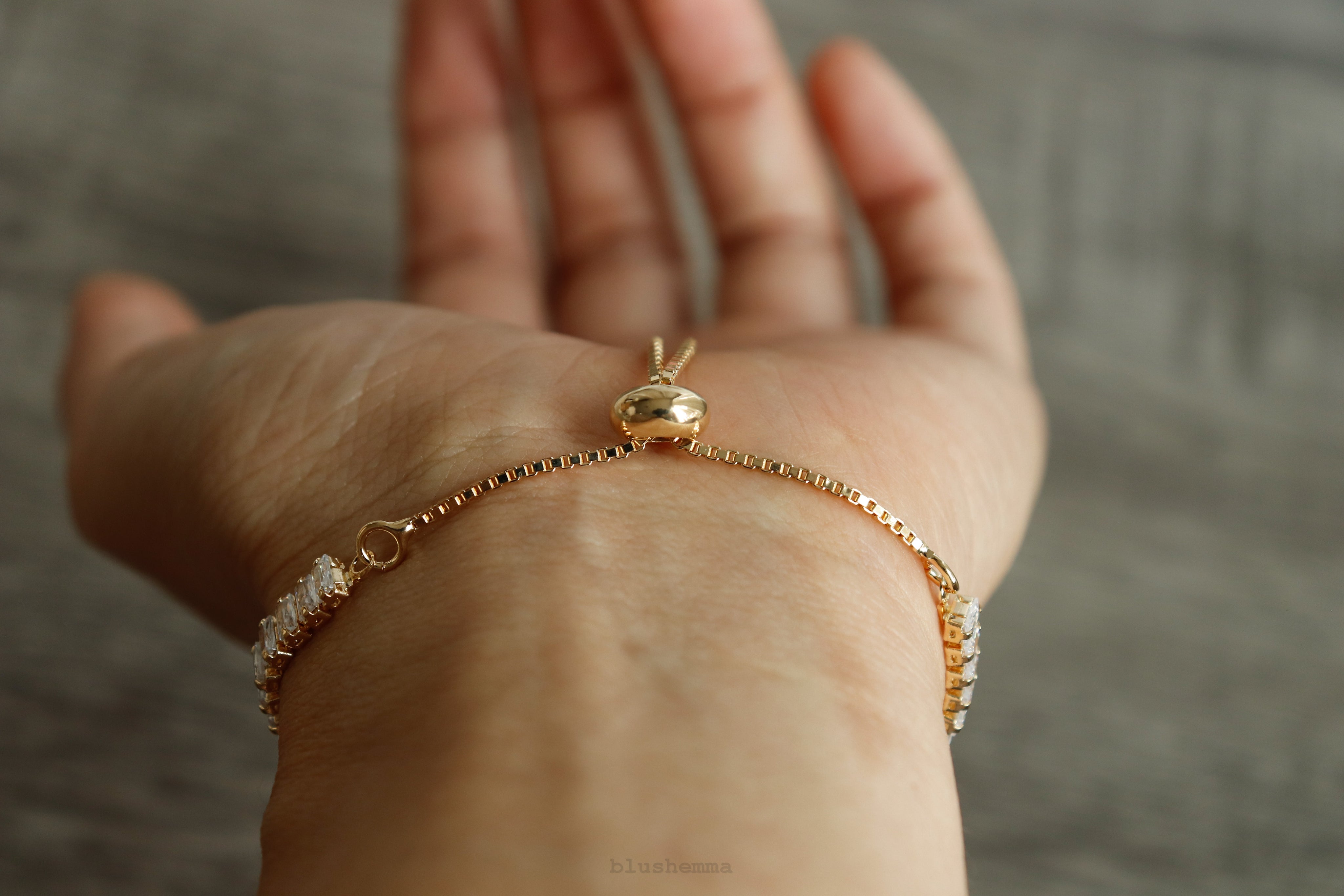 Gold bracelet with a small pendant on a person's wrist against a neutral background