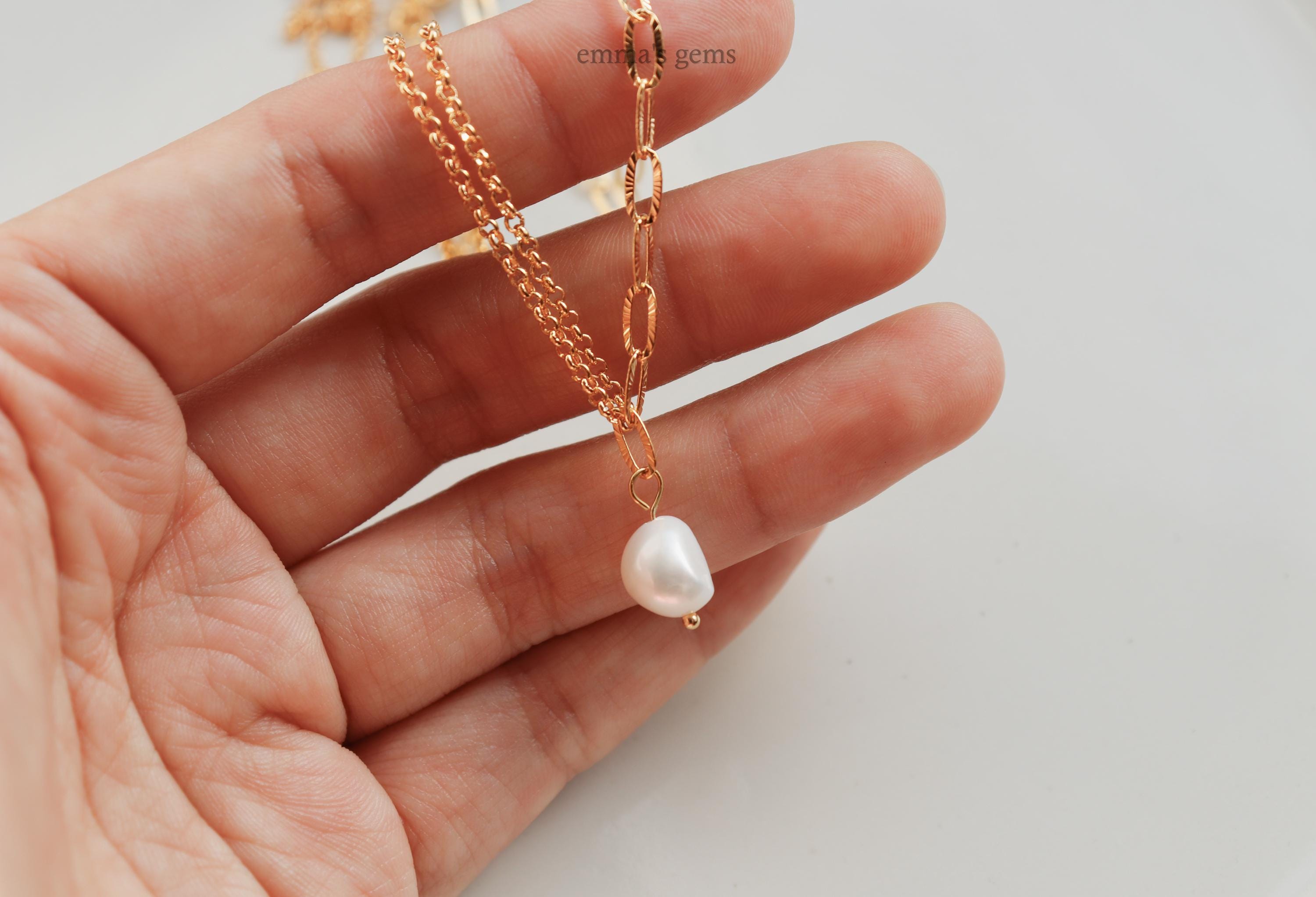 Hand holding a delicate gold chain necklace with a pearl pendant on a light background