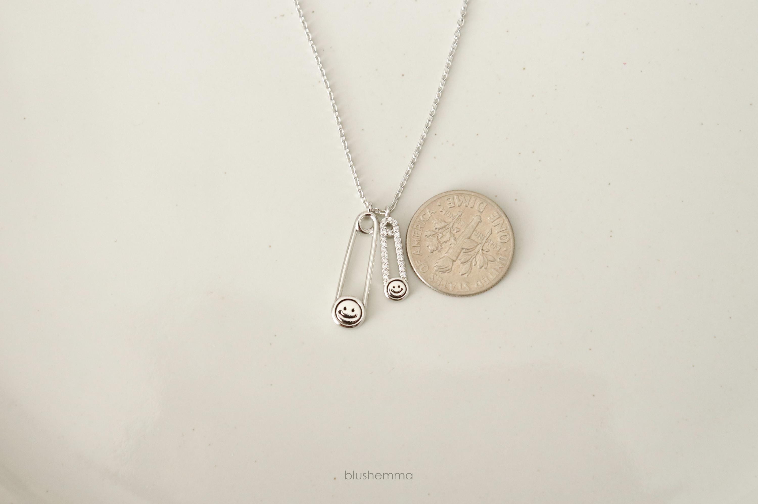 silver Double Safety Pin Charm Necklace. wih dime for scale
Each pin has a Happy Face and the smaller one is cubic paved along pin shape.