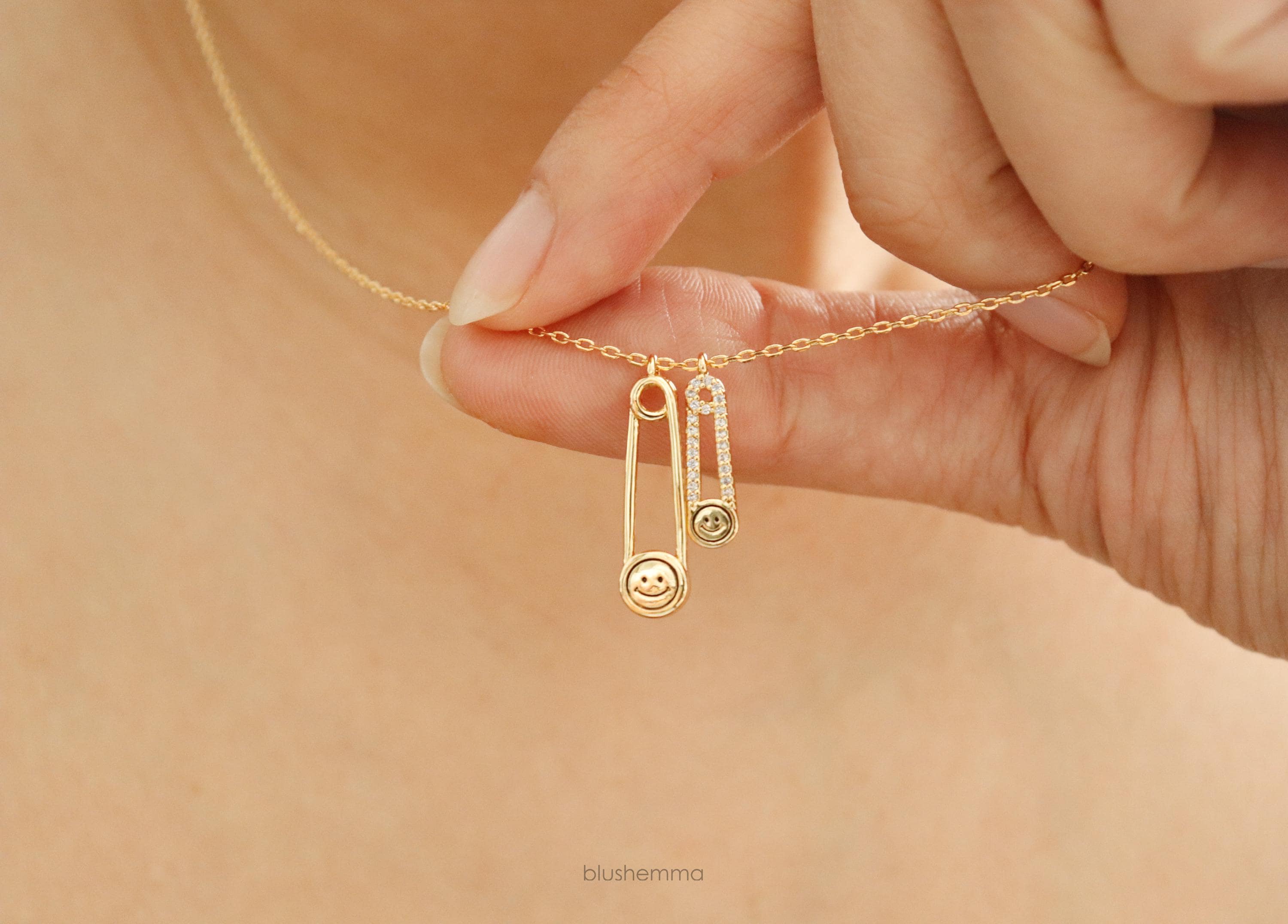 Gold Double Safety Pin Charm Necklace.
Each pin has a Happy Face and the smaller one is cubic paved along pin shape.