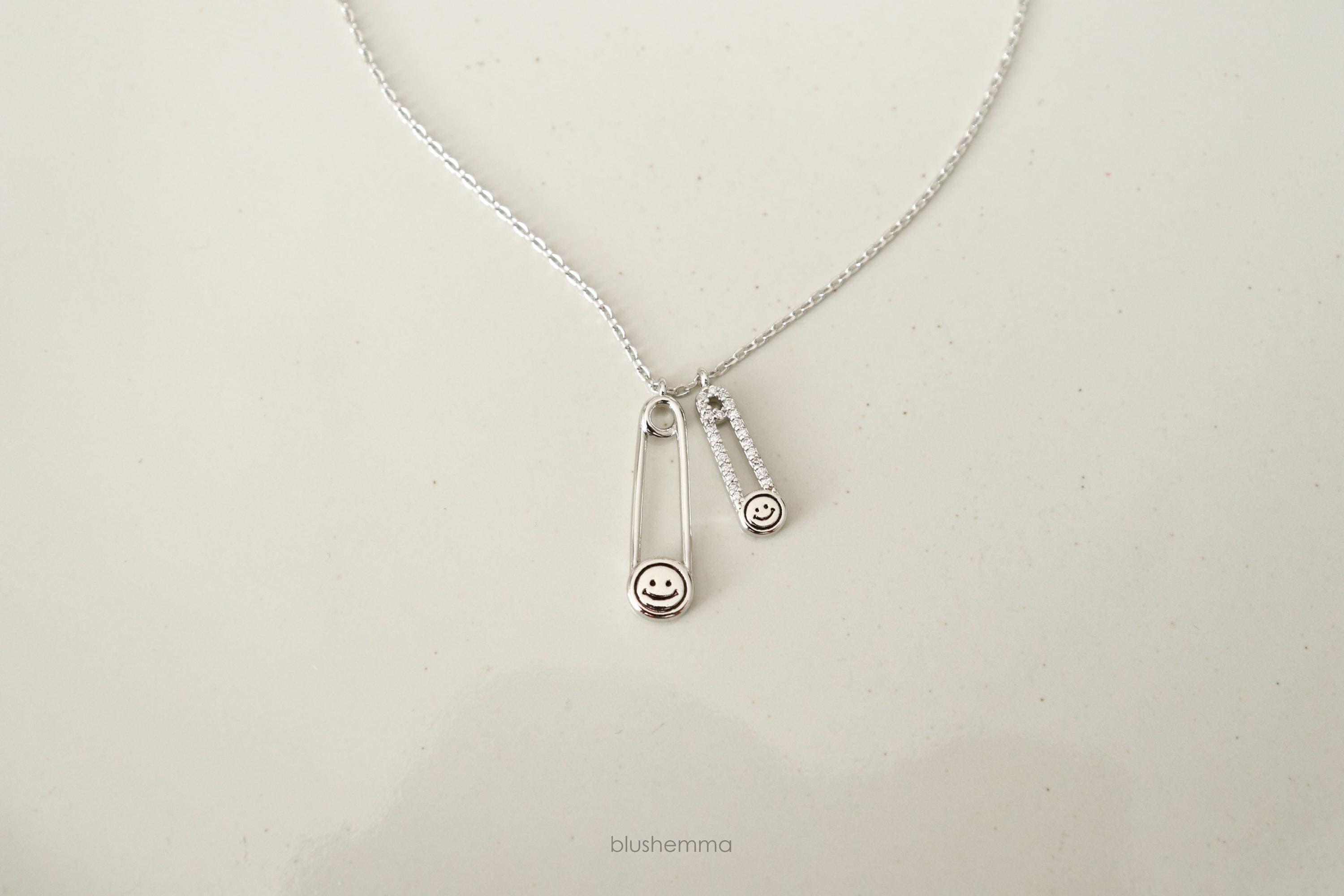 silver Double Safety Pin Charm Necklace.
Each pin has a Happy Face and the smaller one is cubic paved along pin shape.