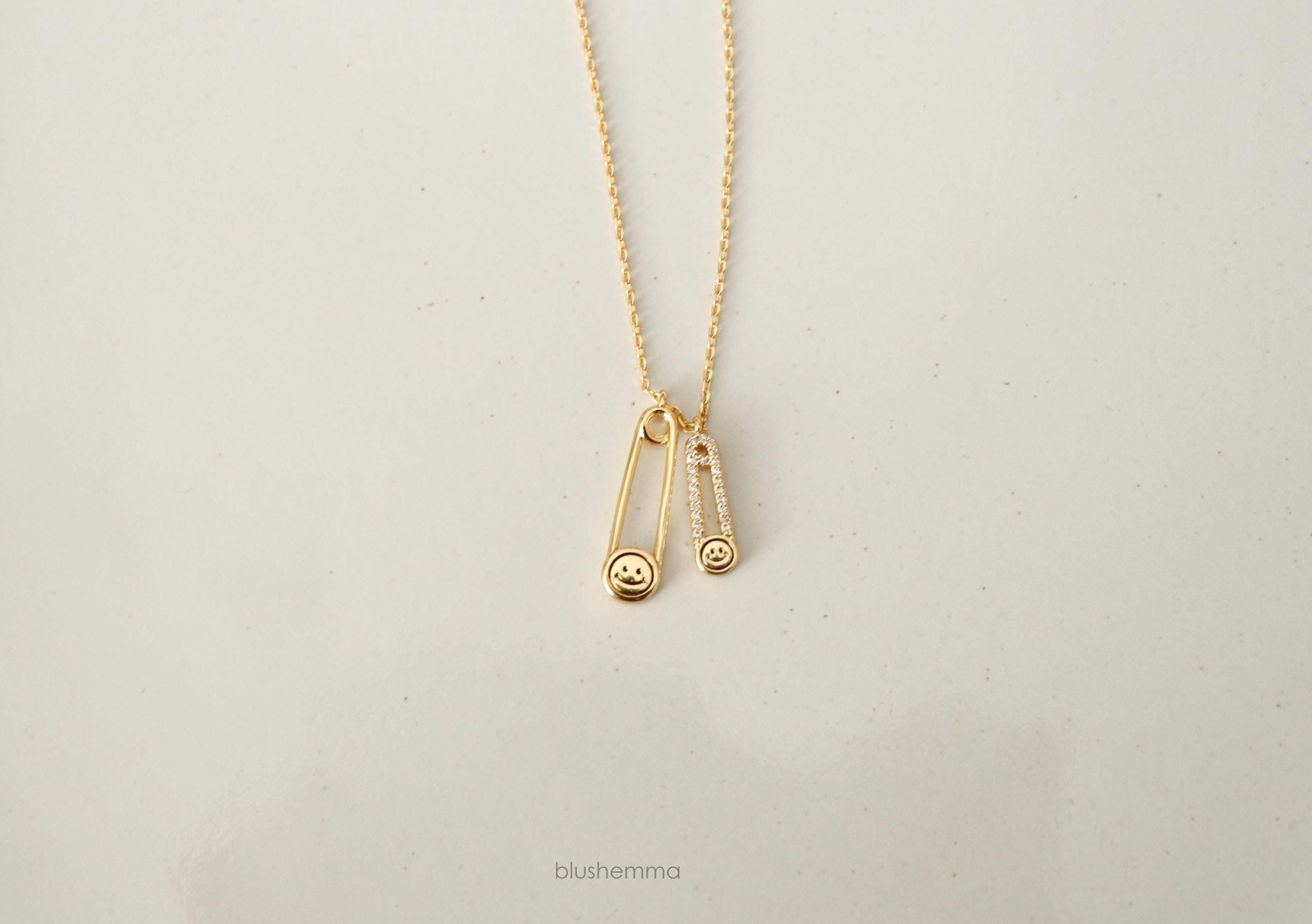 gold Double Safety Pin Charm Necklace.
Each pin has a Happy Face and the smaller one is cubic paved along pin shape.