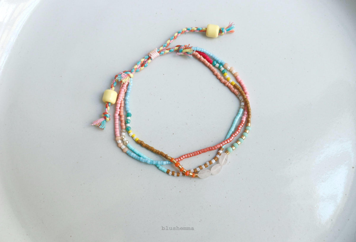 A set of multi-strand beaded friendship bracelets with colorful threads and light yellow wooden beads, arranged on a white plate.